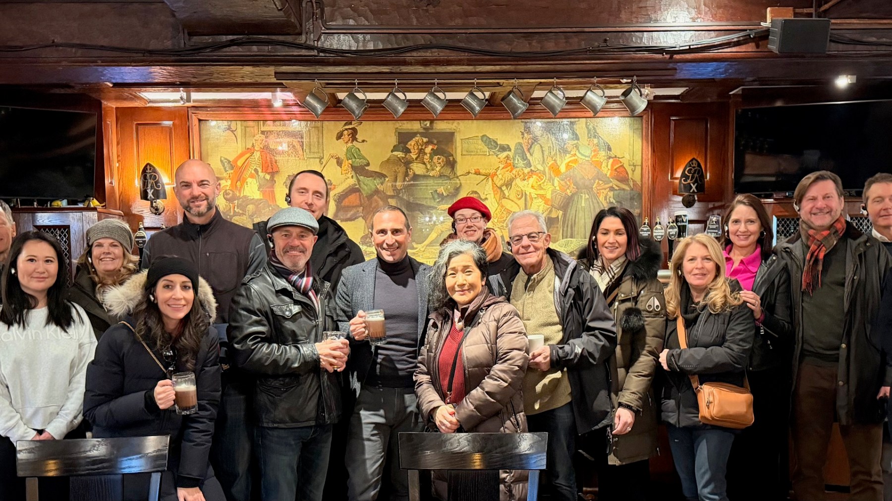 Group of people in winter clothing smiling in a cozy wooden bar interior.