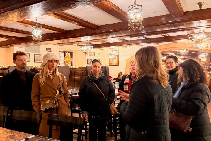 Group of people in warm attire standing inside a restaurant with wooden beams and hanging lights.