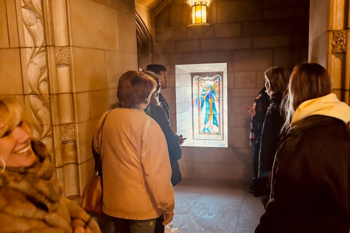 People stand in a stone hallway observing a colorful stained glass window.