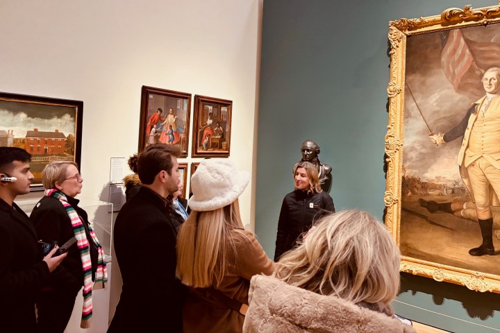 People in a museum gallery observing historic paintings and sculptures.