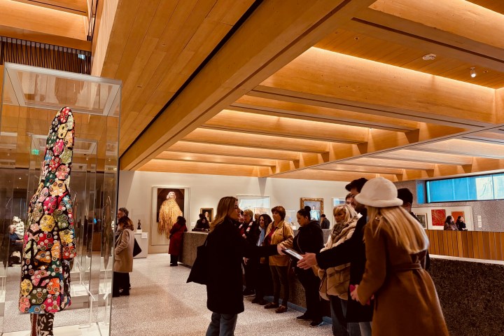 People viewing colorful floral artwork in a modern, wooden-ceilinged gallery.