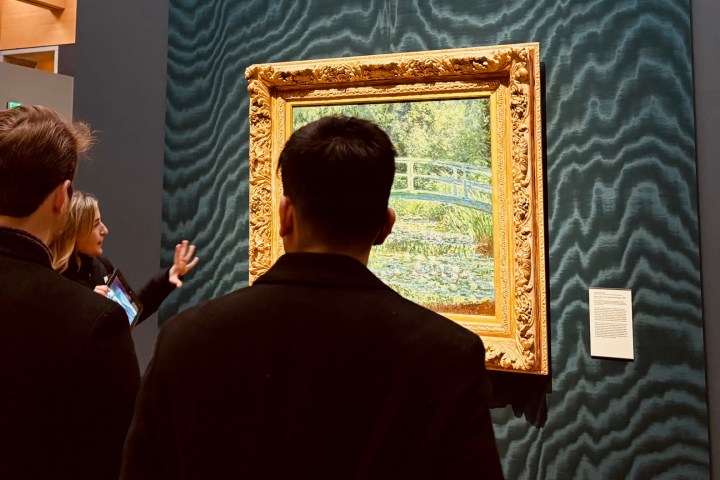 People viewing a framed painting in a museum with an ornate gold frame.
