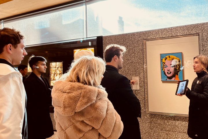 Group of people observing artwork in a gallery, one person holding a tablet.