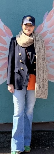 Person in front of angel wings mural with cap, scarf, and jacket.